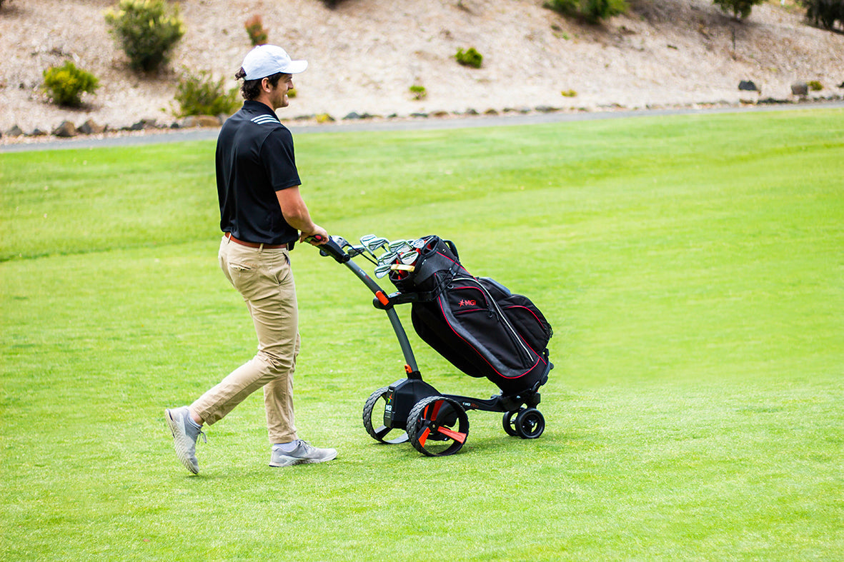Golfer walking the fairway beside an MGI electric golf caddy carrying their bag