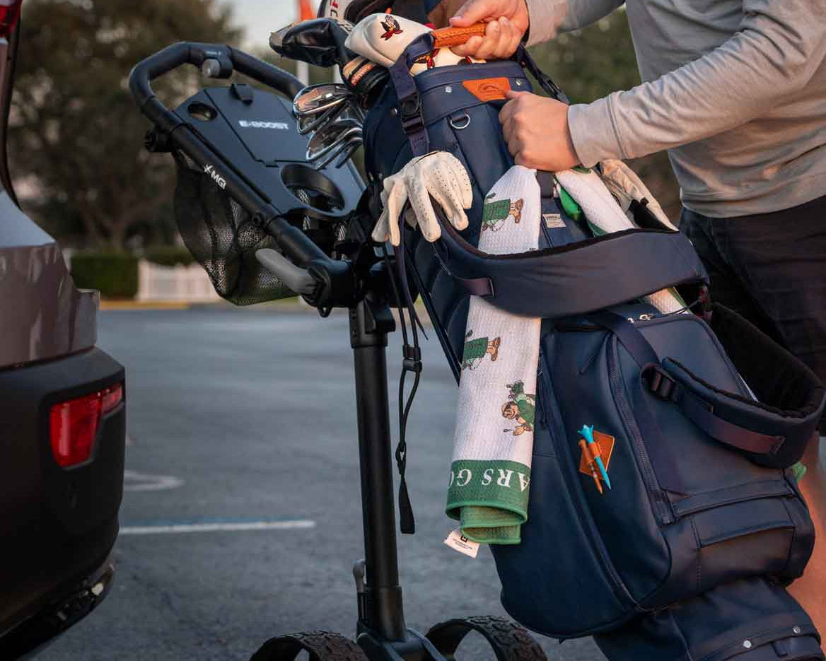Person loading golf equipment into a cart with a car in the background