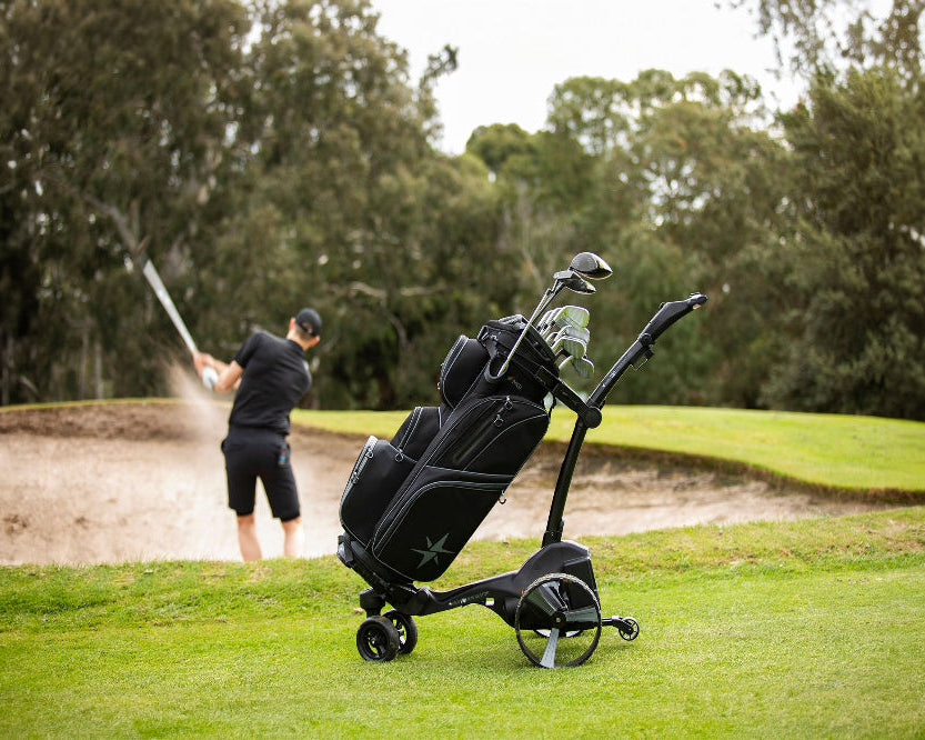 Golf cart with golf bag and clubs on a golf course with a golfer in the background.